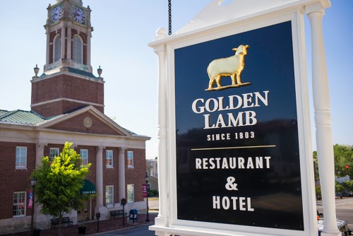 Sign for the Golden Lamb Restaurant & Hotel, featuring a golden sheep, with a historic building in the background.
