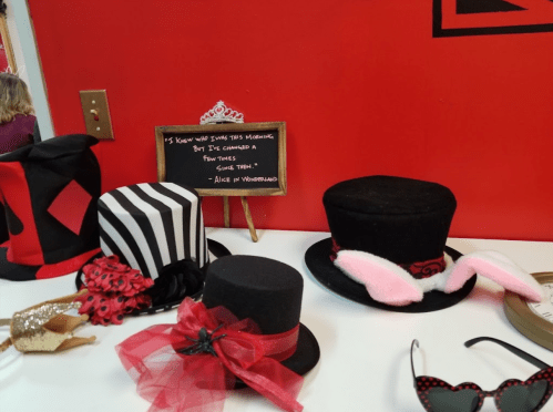 A variety of decorative hats displayed on a table, including a striped top hat and a bunny-eared hat, against a red wall.
