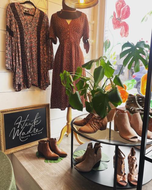 A boutique display featuring dresses, shoes, and a potted plant, with a sign reading "Hawk Made Resale Boutique."