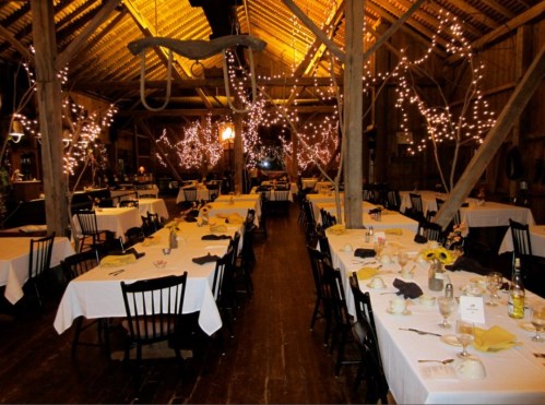 A rustic dining hall with tables set for a meal, adorned with fairy lights and decorated with sunflowers.