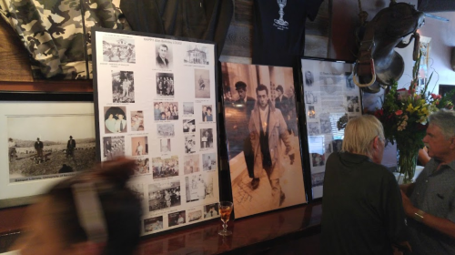 A bar scene featuring historical photos and displays on the walls, with patrons engaged in conversation.