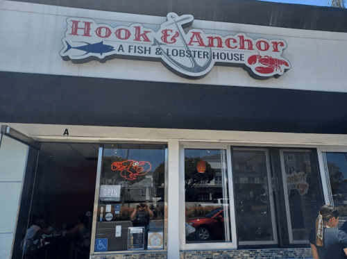 Exterior of Hook & Anchor, a fish and lobster house, featuring a sign and large windows with diners inside.