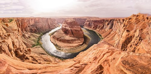 A panoramic view of Horseshoe Bend, showcasing a winding river surrounded by towering red rock formations.