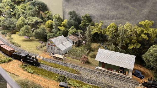 A miniature train scene featuring a small house, barn, and lush greenery along a railway track.