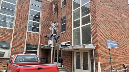 A red pickup truck parked in front of a brick building with a railroad crossing sign and signals.
