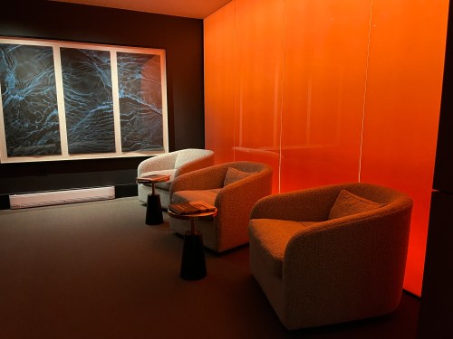 A cozy room with two armchairs, small tables, and an orange-lit wall featuring abstract artwork.