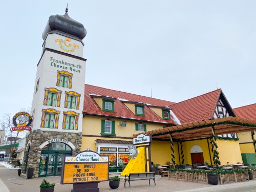 A colorful building with a tower, featuring "Frankenmuth Cheese Haus" signage and outdoor seating.