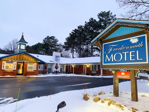 A snowy scene featuring the Frankenmuth Motel with a "No Vacancy" sign and surrounding trees.