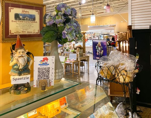 A decorative gnome stands beside a sign and a display of baked goods in a cozy shop setting.