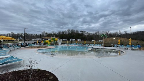 A cloudy day at a pool area with lounge chairs, umbrellas, and a palm tree, surrounded by green hills.