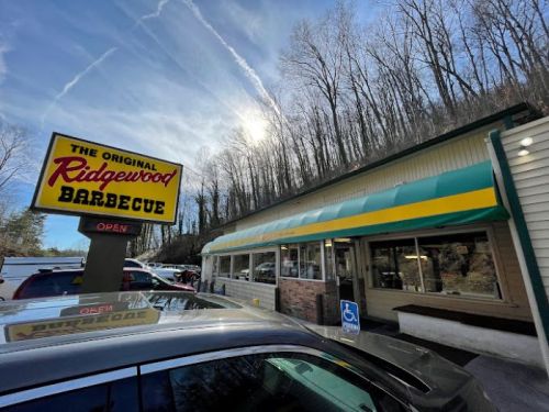 Exterior of Ridgewood Barbecue restaurant with a bright sign, surrounded by trees and a clear sky.