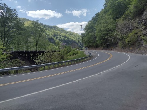 A winding road curves through lush green hills under a partly cloudy sky.