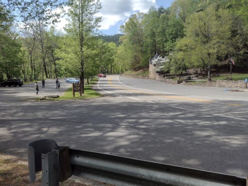 A scenic view of a park entrance with trees, a road, and a few people walking in the distance.