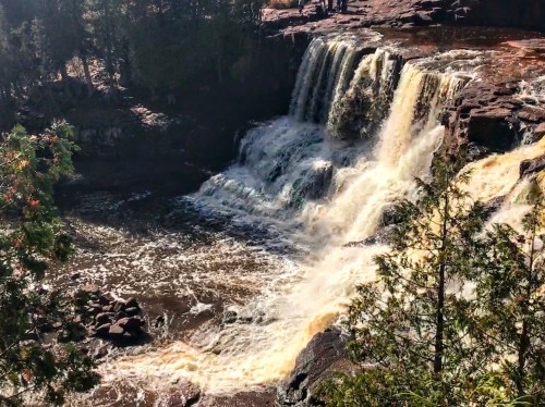 A scenic waterfall cascading over rocks, surrounded by trees and a flowing river below.