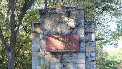 Sign for Dammel State Park, mounted on a stone structure, surrounded by trees and greenery.
