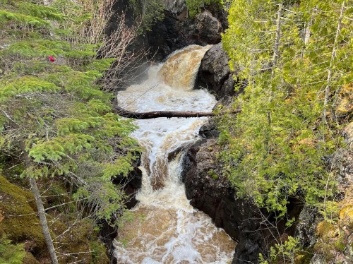 A rushing waterfall cascades through rocky terrain, surrounded by lush green trees and foliage.