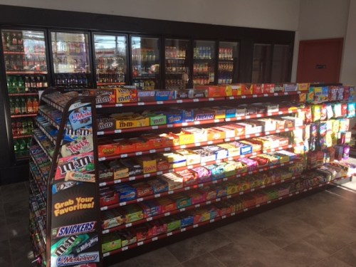 A brightly lit convenience store snack aisle filled with various candy and snack options on display.