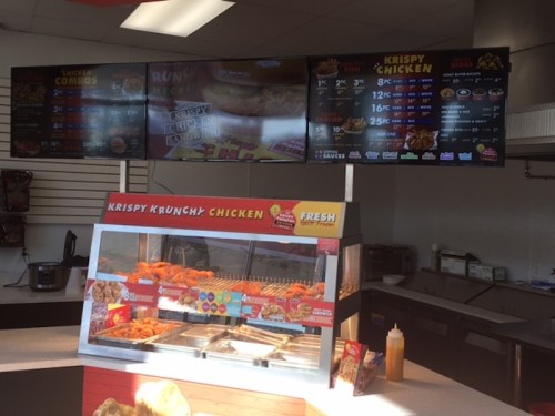Interior of a fast-food restaurant featuring a menu board and a display case with fried chicken.