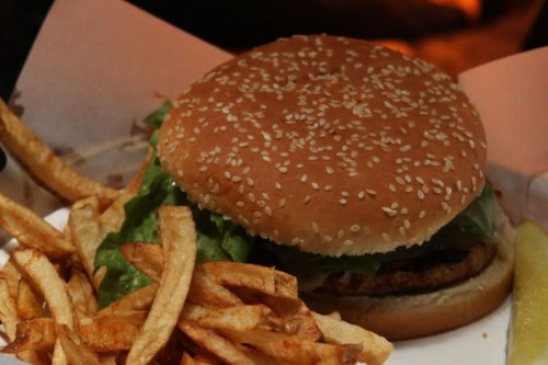 A sesame seed bun burger with lettuce, served alongside crispy French fries and a slice of lemon.