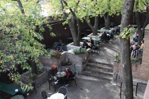 A cozy outdoor café with green trees, tables, and people enjoying their meals in a relaxed setting.