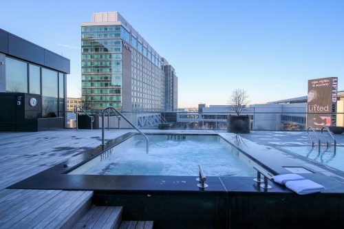 Rooftop hot tub with a view of a modern building and clear blue sky.