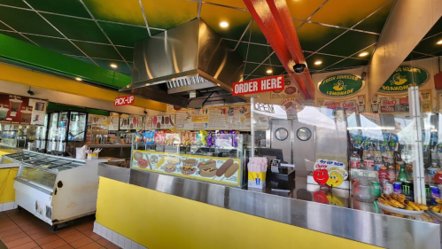 Colorful food counter with signs for "Order Here" and "Pick-Up," showcasing various snacks and drinks.