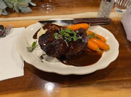 A plate of beef with a rich sauce, served with mashed potatoes and glazed carrots, garnished with microgreens.
