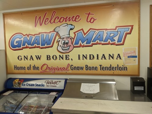 Sign for Gnaw Mart in Gnaw Bone, Indiana, featuring a cartoon chef and promoting the original Gnaw Bone tenderloin.
