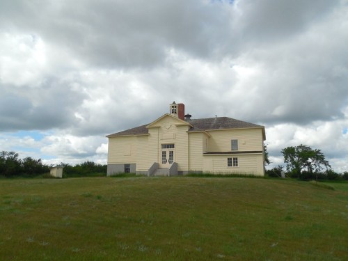 A large, yellow house sits on a grassy hill under a cloudy sky.