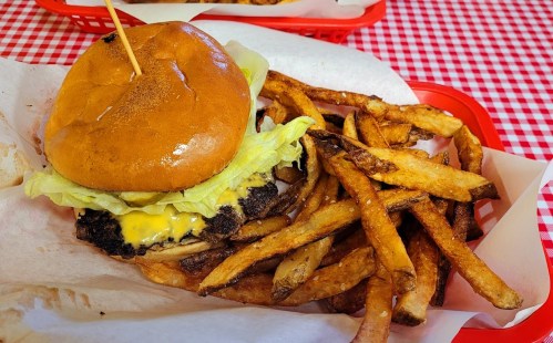 A cheeseburger with lettuce on a bun, served with a side of golden-brown French fries in a red basket.