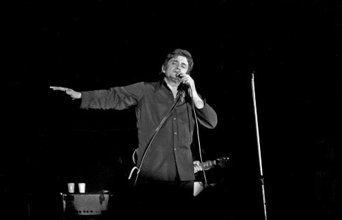 A singer performs on stage, microphone in hand, with a spotlight illuminating him against a dark background.