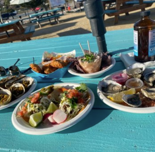 A colorful spread of seafood dishes, tacos, and sauces on a turquoise table at a beachside setting.