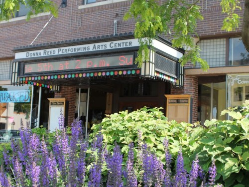 Entrance of the Donna Reed Performing Arts Center, featuring colorful signage and vibrant flowers in the foreground.
