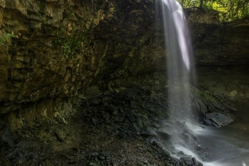 A serene waterfall cascading over rocky cliffs into a calm pool below, surrounded by lush greenery.