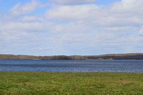 A serene lake surrounded by green grass and trees under a partly cloudy sky.