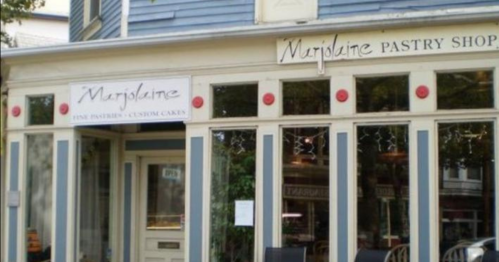 Exterior of Marjolaine Pastry Shop, featuring large windows and a welcoming entrance with signs for pastries and custom cakes.
