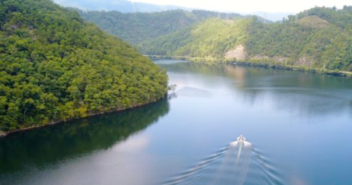 Aerial view of a serene lake surrounded by lush green hills and a boat leaving ripples in the water.