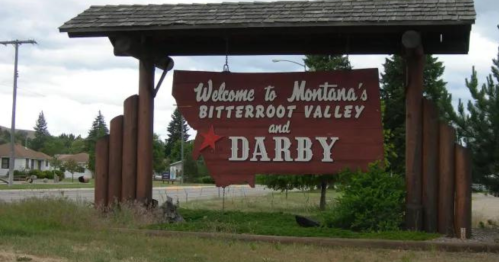 Sign welcoming visitors to Montana's Bitterroot Valley and Darby, framed by trees and a cloudy sky.