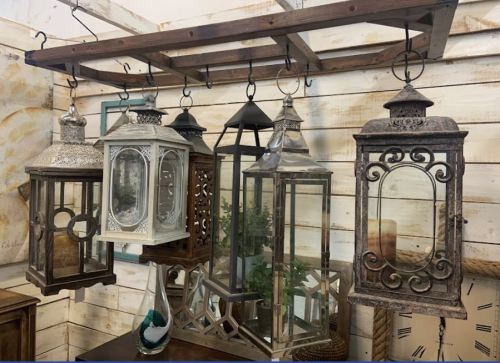 A collection of decorative lanterns hanging from a wooden rack against a rustic wall.