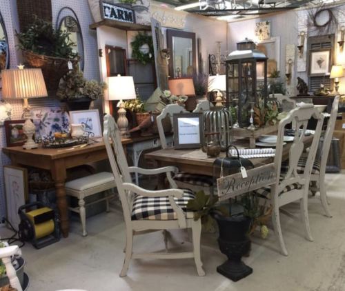 A cozy vintage-inspired room featuring a wooden dining table, chairs, lamps, and various decorative items.