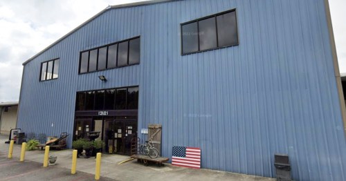 A large blue industrial building with a glass entrance and an American flag displayed outside.