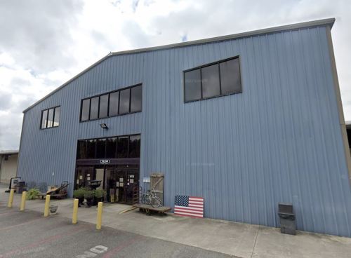 A large blue metal building with multiple windows and an entrance, featuring an American flag near the door.