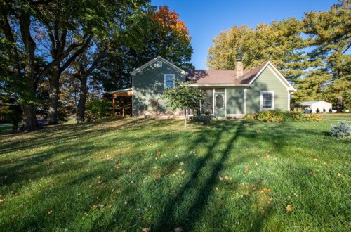 A green house surrounded by trees and a grassy yard, with autumn foliage and clear blue skies.