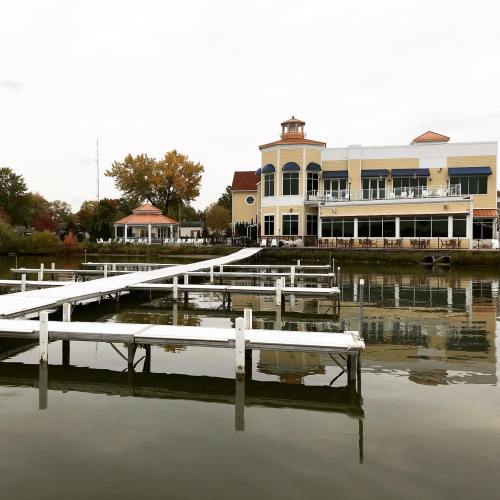 A wooden dock extends over calm water, leading to a large, elegant building with a blue and yellow facade.