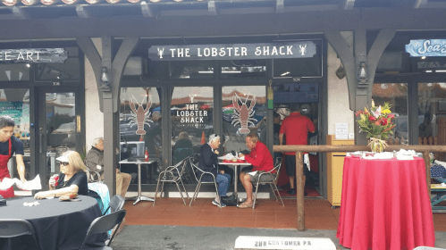 Exterior of The Lobster Shack restaurant, featuring a sign, outdoor seating, and patrons enjoying their meals.