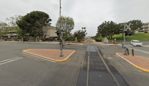 A quiet intersection with railroad tracks, traffic signals, and greenery in the background on an overcast day.