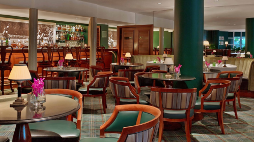 A stylish restaurant interior with wooden chairs, tables, and a bar in the background, featuring soft lighting and floral decor.