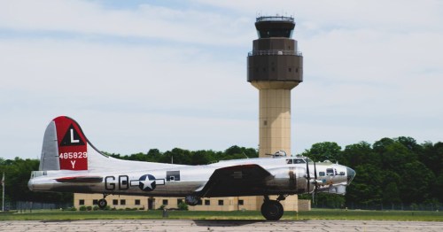 A vintage B-17 bomber taxiing on an airfield with a control tower in the background.