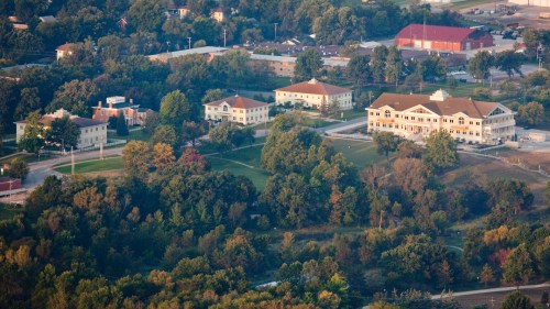 Aerial view of a suburban area with several buildings, trees, and green spaces, showcasing a mix of residential and commercial structures.