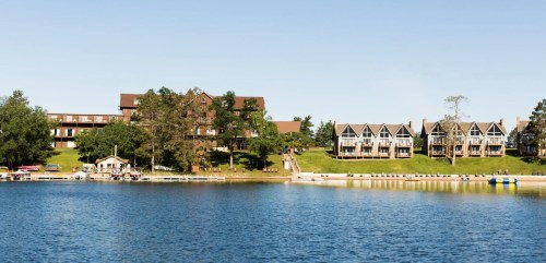 Scenic view of a lake with waterfront buildings and greenery under a clear blue sky.